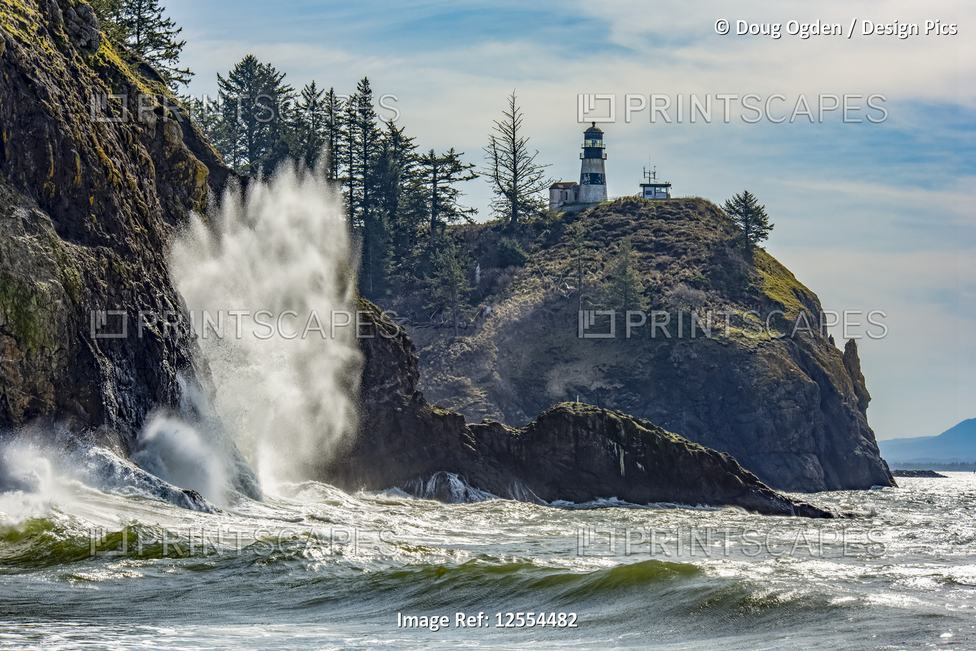 A wave crashes on the rocks below the Cape Disappointment North Head Lighthouse ...