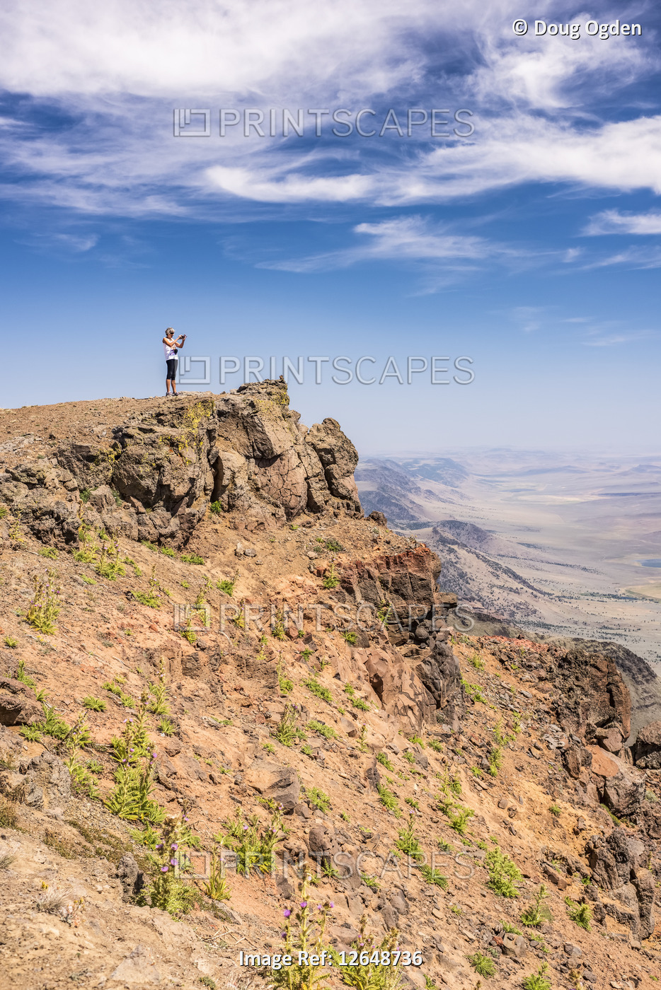 A woman looking out across the Alvord Desert from a cliffs edge on Steens ...