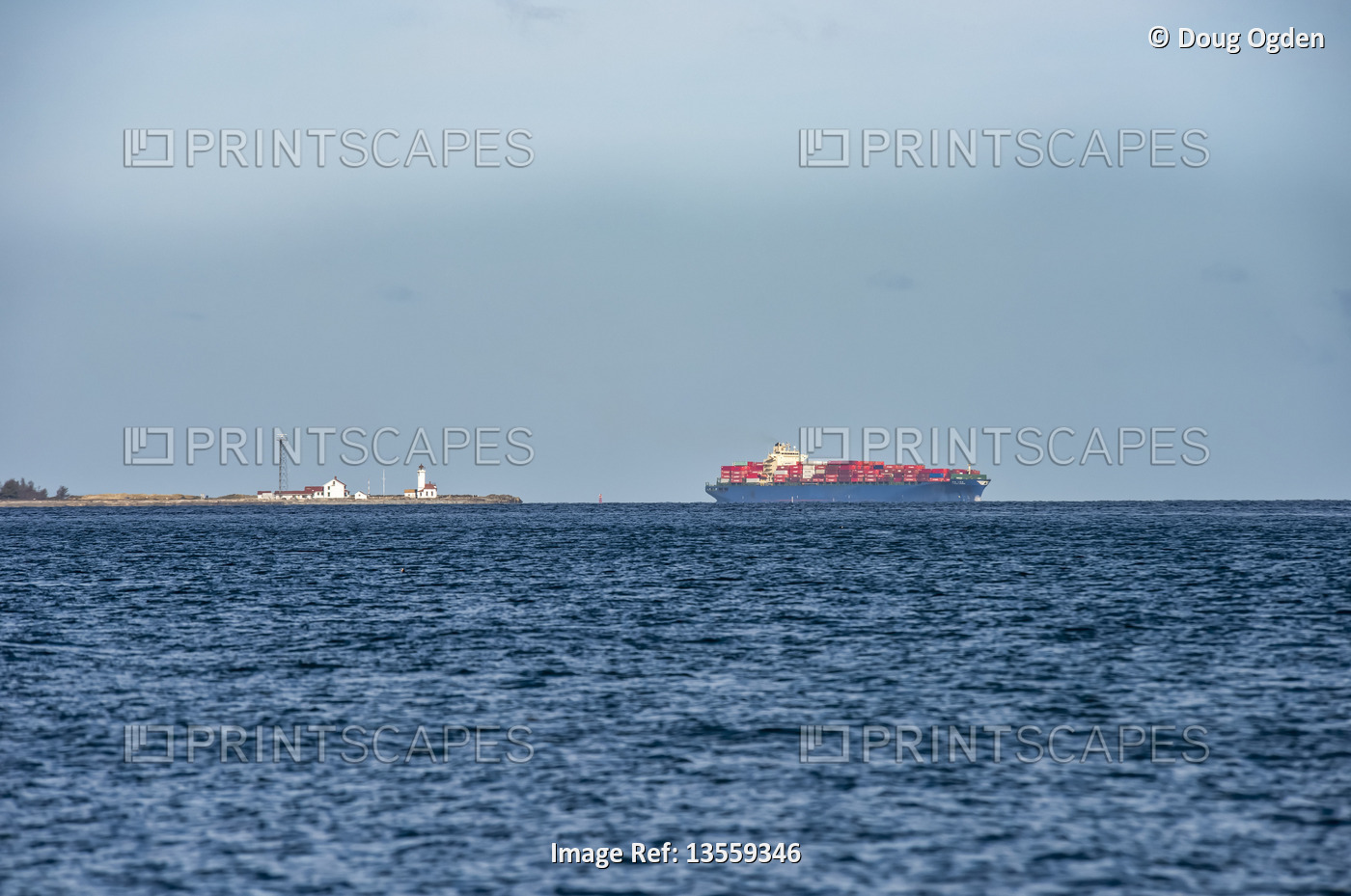 Cargo Ship and lighthouse viewed from Marrowstone Island with blue ocean water ...